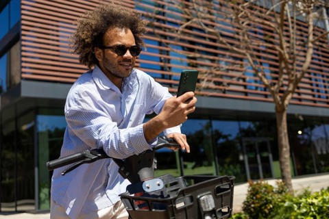 A stylish man with an afro hairstyle enjoys a sunny day while riding an electric bicycle. He is