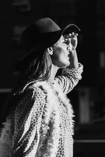 A stylish woman in a hat poses in black and white, capturing sunlight with elegance and grace. Her