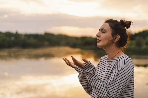 A serene moment captured as a woman praying in a striped sweater enjoys a peaceful sunset by the