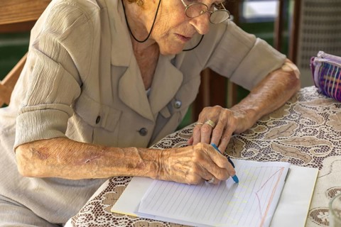 Senior woman wearing eyeglasses is carefully drawing colorful lines and curves on a notebook with