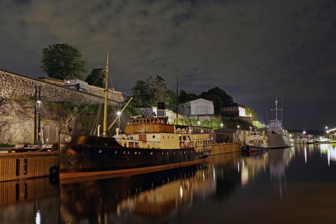 Harbour scene at night with old and new ships reflected in the water, old fortress in the