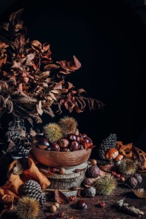 A beautifully arranged autumn scene featuring a bowl of chestnuts, surrounded by dried leaves, pine