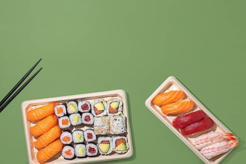 Top down view of assorted sushi in eco friendly trays, set against a modern green backdrop. Perfect