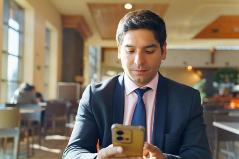 Young Chilean businessman in a contemporary cafe, wearing a suit and using a smartphone. Sunlight