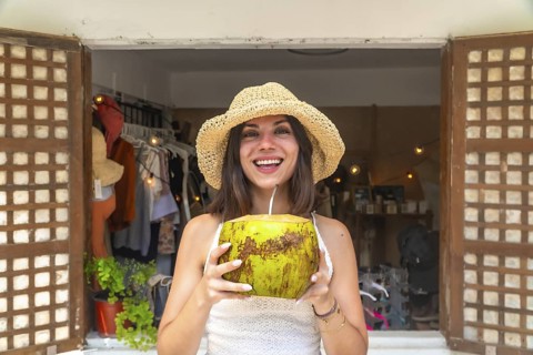 Young woman with straw hat drinking fresh coconut water in front of a shop in siargao island,