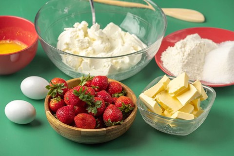Fresh baking ingredients, including strawberries, butter, sugar and quark, on a green background