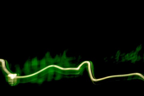 Vivid green light trails weave through a dark space, creating an abstract visual journey. The