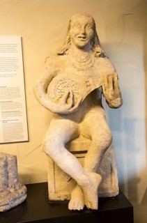 Female carved stone figure playing lute in museum at Bruton, Somerset, England, UK