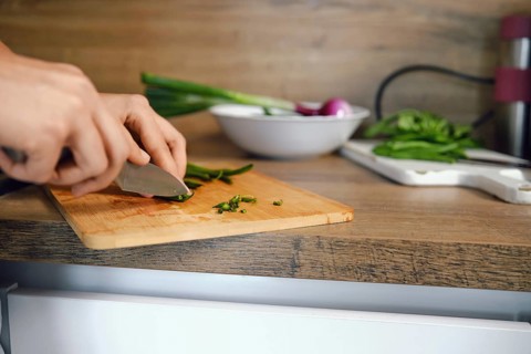Close-up view of trimming ends of green beans with knife on chopping board. Fresh vegetables are on