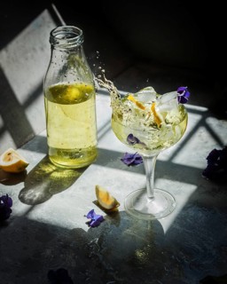 Lemon liqueur in a glass, with ice cubes and lemon slices, splashes dramatically in sunlight.