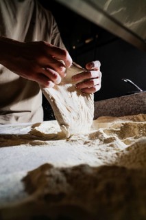 Close up of skilled hands stretching freshly kneaded dough on a floured surface in a warm, ambient