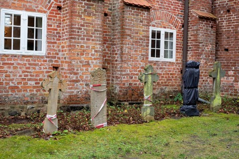 Old gravestones in front of a red brick wall with ecclesiastical windows in the background,