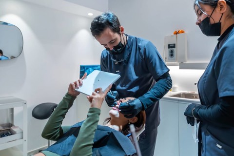 Dentist showing teeth whitening results to a patient on a digital tablet, assisted by a dental