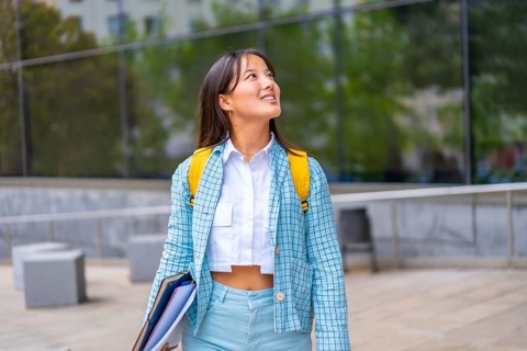 Happy asian student looking up with hopeful expression outside the university