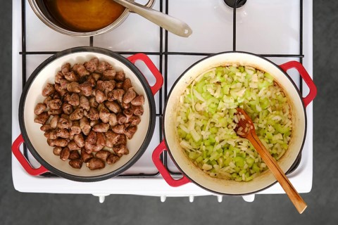 A stove top displays two pans. One pan has cooked chicken hearts while the other holds sauteed