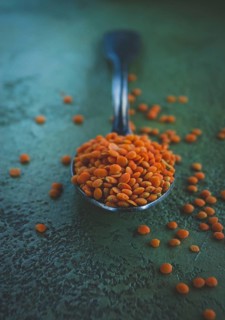 A spoon rests on a textured surface, holding a mound of vibrant orange lentils. Some lentils