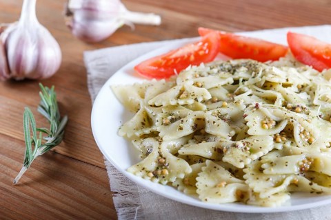 Farfalle pasta with pesto sauce, tomatoes and cheese on a linen tablecloth on a brown wooden