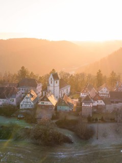Rural village in the morning sun with church and half-timbered houses against a backdrop of hills,