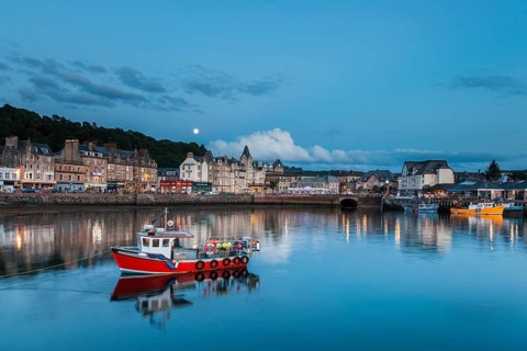 UK. Scotland. Argyll and Bute. Oban. Red fishing boat in the port of Oban with the town in the