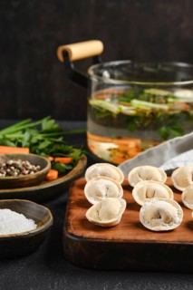 Dumplings are neatly arranged on a wooden board alongside vibrant fresh herbs and spices. A pot of