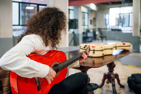 Latin man with long hair playing red bass guitar in studio