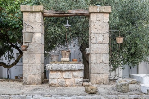 Old stone fountain in a Mediterranean garden with buckets and ropes, surrounded by trees, Apulia,