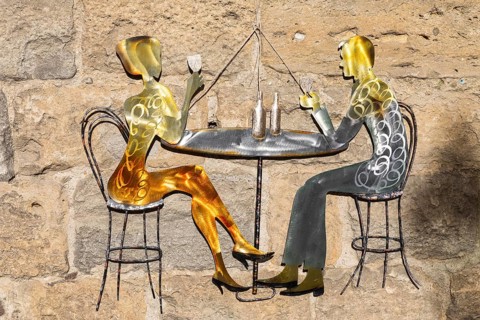 Metal advertising sign of a wine-drinking couple on a house wall in the historic centre of
