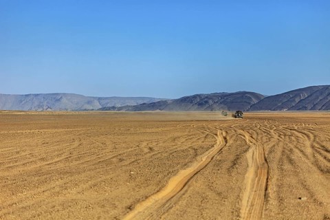 Jeep drives through dusty, barren desert with mountain formations, Off-road vehicle through the