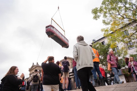 Many on the station forecourt as an old suspension railway wagon is lifted with a truck-mounted
