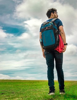 Low angle of traveler man walking in the field. Backpacker man walking in the countryside. Young