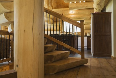 Twisting staircase with wooden and black wrought iron handrail and brown stained half log steps