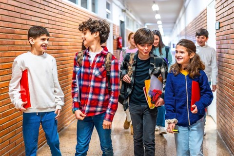 Cheerful students carrying folders and backpacks are walking together down school hallway after