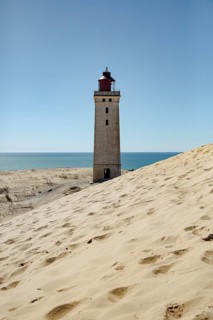 A lighthouse on the coast, surrounded by dunes, with the sea on the horizon, lighthouse in the
