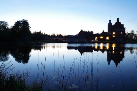 A castle at dusk reflected in a quiet lake with glowing windows, Broholm, Funen, manor house route,