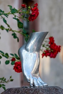 Foot of a woman on tiptoe, silver-coloured sculpture, shiny metallic, red roses in the background,