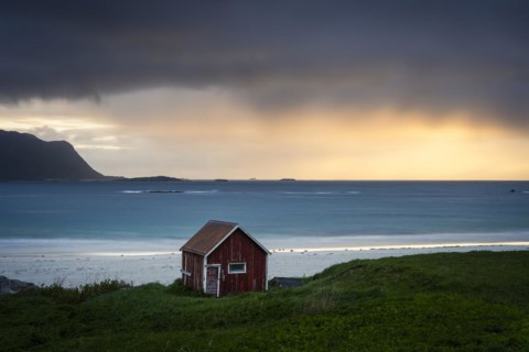 A red wooden hut on the sandy beach of Ramberg (Rambergstranda), with the sea behind it. At night