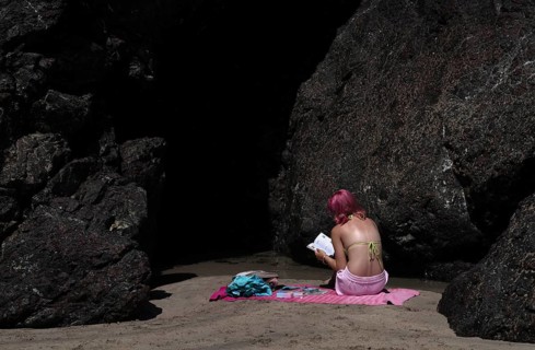 Girl, woman, from behind, in bikini, hair mauve, purple, sitting between rocks on bath towel, pink,