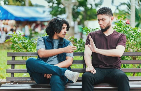 Disgusted guy sitting refusing a cigarette. Young man sitting refusing a cigarette in the park