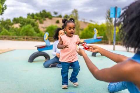 Baby african girl walking to her mother to pick a toy in a public park