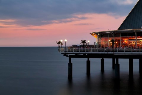 Illuminated restaurant terrace with tourists, Heringsdorf pier at dusk, long exposure, Baltic