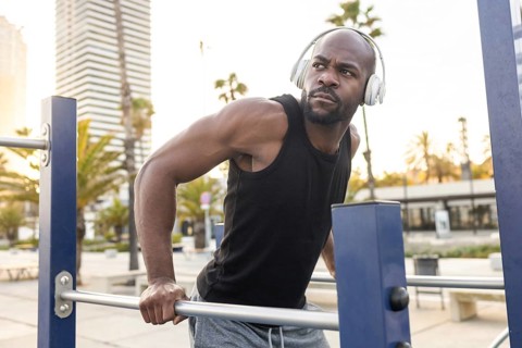 Cuban man in a black tank top works out at an outdoor fitness park, gripping parallel bars. He