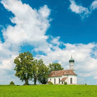 Church of St Andrew on a green meadow under a blue sky with cumulus clouds, also St Andrä,