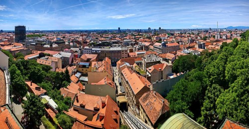 Panoramic view from Lotrscak Tower over a city with tiled roofs and an urban skyline surrounded by