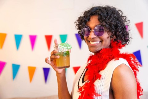 Cool young latin man holding cocktail glass and smiling at camera partying at home