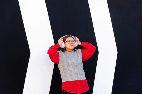 A Latina woman is standing in front of a striking black and white geometric wall, wearing a red