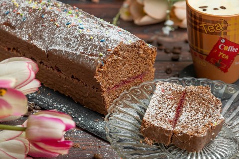 Chocolate cake dusted with icing sugar next to coffee on a wooden table with flowers