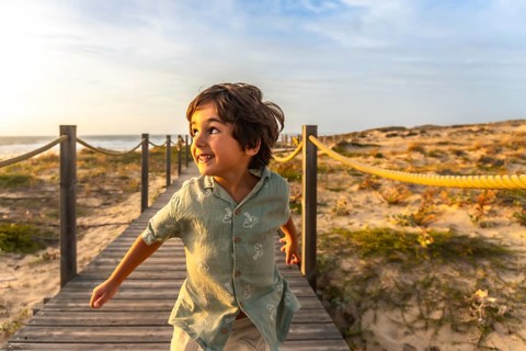 Happy young boy running along a wooden boardwalk over sand dunes at sunset in seignosse, france,