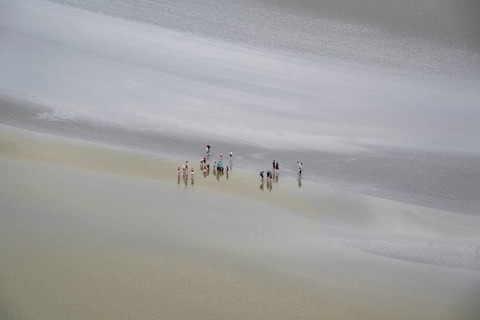 Guided groups of people hiking in a mudflats at low tide in Mont Saint Michel Bay, Pontorson,