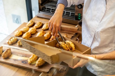 Baker's hands using tongs to carefully place traditional empanadas from a wooden serving board into