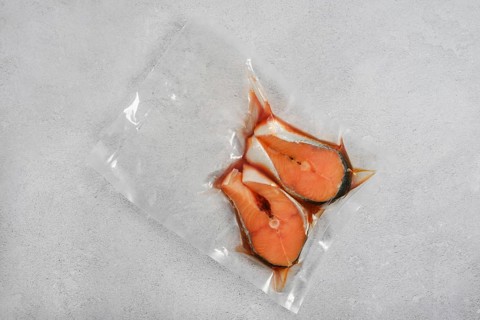 Salmon slices in clear vacuum plastic package on light grey surface. This packaging shows the fish